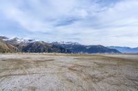 a sandy field with mountains on both sides, a few rocks and grass in the middle