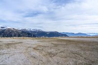 a sandy field with mountains on both sides, a few rocks and grass in the middle