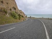 a winding highway with a very steep cliff in the background and ocean in the foreground