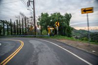 a winding roadway near a green hill under a cloudy sky with many street signs on it