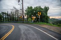 a winding roadway near a green hill under a cloudy sky with many street signs on it