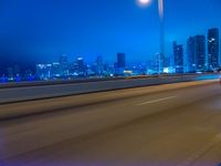 a big city at night with a blue sky above and a large car passing on the road