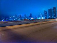 a big city at night with a blue sky above and a large car passing on the road