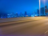 a big city at night with a blue sky above and a large car passing on the road