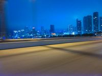 a big city at night with a blue sky above and a large car passing on the road