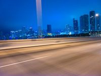 a big city at night with a blue sky above and a large car passing on the road