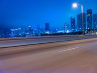 a big city at night with a blue sky above and a large car passing on the road