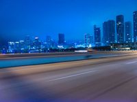 a big city at night with a blue sky above and a large car passing on the road