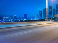 a big city at night with a blue sky above and a large car passing on the road