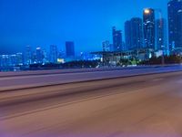 a big city at night with a blue sky above and a large car passing on the road