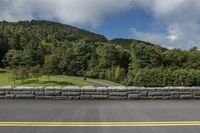 the motorcycle is stopped at the side of the road near a stone wall and hill