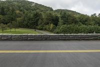 the motorcycle is stopped at the side of the road near a stone wall and hill