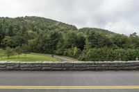 the motorcycle is stopped at the side of the road near a stone wall and hill