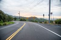 a curve in the road with a street sign on it's side and mountain area on the other side