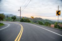 a curve in the road with a street sign on it's side and mountain area on the other side