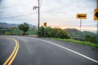 a curve in the road with a street sign on it's side and mountain area on the other side