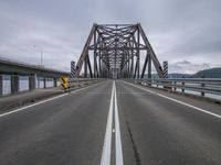 a truck drives down the empty road with a bridge behind it in a cloudy day