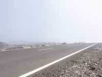 a road near the mountain side in the foggy sun day, and on the opposite bank are hills