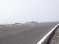 a road near the mountain side in the foggy sun day, and on the opposite bank are hills