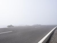 a road near the mountain side in the foggy sun day, and on the opposite bank are hills