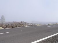 a road near the mountain side in the foggy sun day, and on the opposite bank are hills