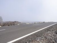 a road near the mountain side in the foggy sun day, and on the opposite bank are hills