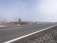 a road near the mountain side in the foggy sun day, and on the opposite bank are hills