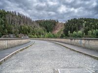 concrete walkway with trees and fenced in area on opposite sides of the road and one side of the road