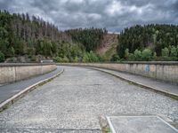 concrete walkway with trees and fenced in area on opposite sides of the road and one side of the road