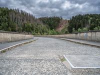 concrete walkway with trees and fenced in area on opposite sides of the road and one side of the road