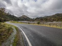 a lone road is empty on a stormy day along a mountain side in the distance is a river