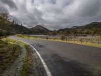 a lone road is empty on a stormy day along a mountain side in the distance is a river