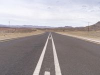 the empty road in the desert with two white lines down the middle of it, as if in the sky