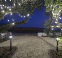 the lighting is glowing around the large courtyard area of this home and courtyard, along with a paved pathway