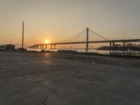 the sun is setting behind a bridge over water and boats docked on the dock and in the bay area