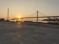 the sun is setting behind a bridge over water and boats docked on the dock and in the bay area