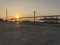 the sun is setting behind a bridge over water and boats docked on the dock and in the bay area