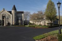 a building with a gothic roof is next to a road and lawn with bushes, shrubs, and bushes