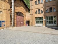 graffiti and bricked walkway outside an old building with open doors and windows at the side