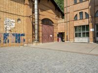 graffiti and bricked walkway outside an old building with open doors and windows at the side