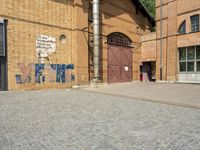 graffiti and bricked walkway outside an old building with open doors and windows at the side