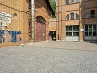 graffiti and bricked walkway outside an old building with open doors and windows at the side