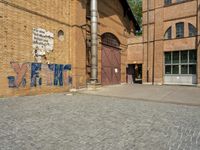 graffiti and bricked walkway outside an old building with open doors and windows at the side