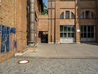 graffiti and bricked walkway outside an old building with open doors and windows at the side