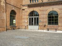 graffiti and bricked walkway outside an old building with open doors and windows at the side