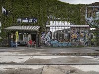 a graffiti covered building in front of some water and green leaves on it's walls