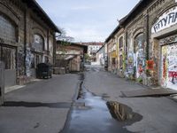 graffiti covered buildings line a empty, narrow alley lined with potholes and abandoned buildings