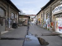 graffiti covered buildings line a empty, narrow alley lined with potholes and abandoned buildings