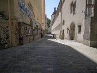 a cobblestone street with a clock tower on it and graffiti all over the wall