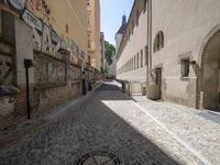 a cobblestone street with a clock tower on it and graffiti all over the wall